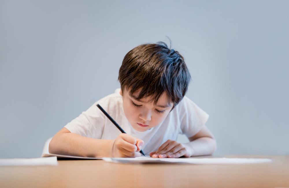 Kid holding pencil writing on white paper child boy is drawing portrait of school kid doing homework alone elementary homeschooling new normal life style children learning at home
