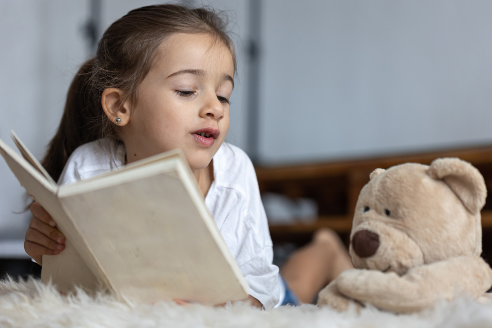 little girl at home, lying on the floor with her favorite toy and reads book.
